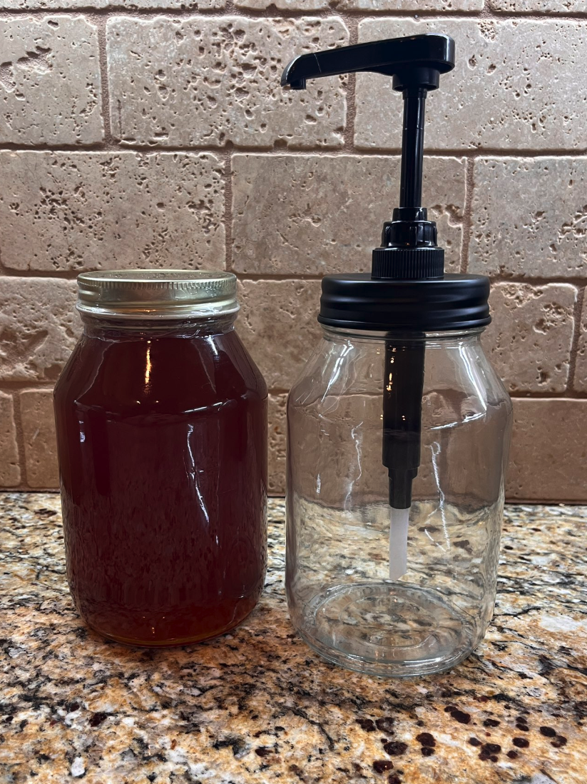 honey pump in glass jar of honey next to a full honey jar